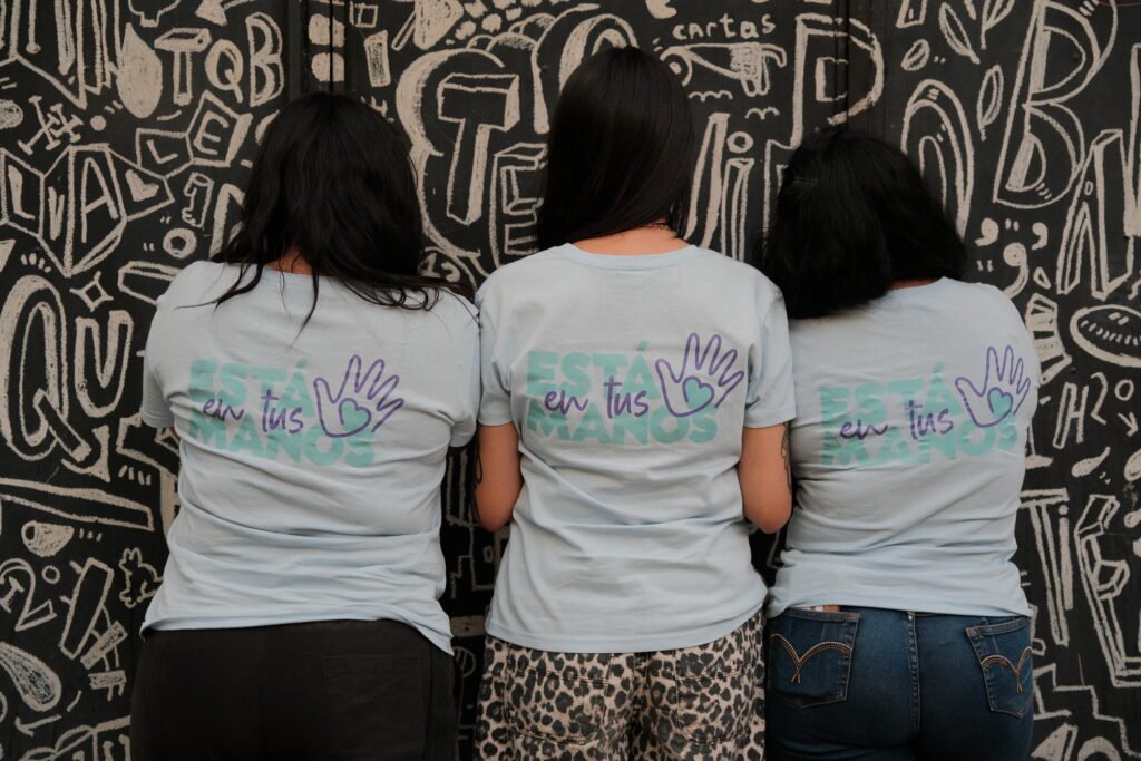 Three volunteers from behind wearing ‘Est&aacute; en tus manos’ campaign shirts
